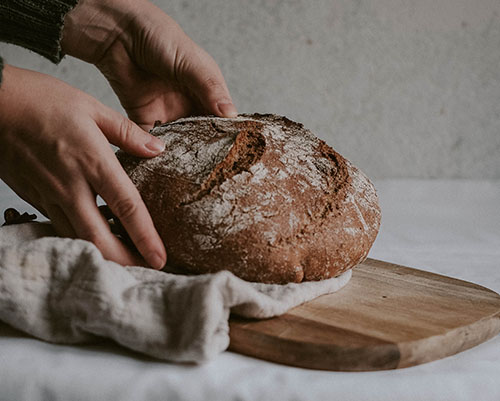 A pair of hands place a handmade bread loaf on a wooden board.