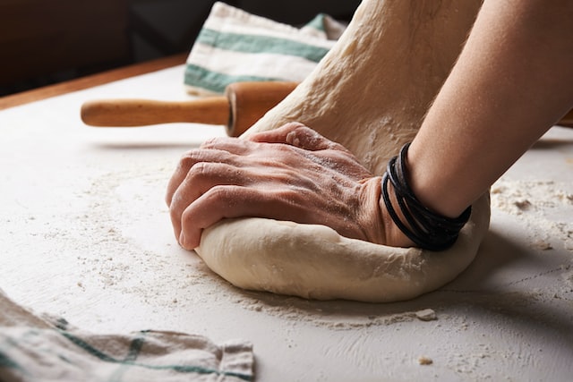 A pair of hands knead dough on a floured surface.