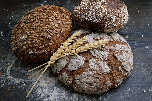 An image of three rustic loaves, with an ear of corn.