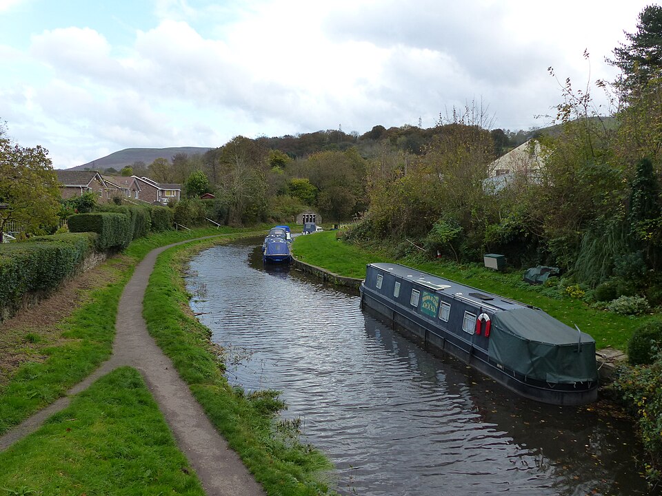 A canal cuts through the centre of the image. A narrow tow path runs along the lefthand bank, and canal boats are moored on the righthand bank.